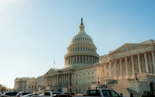 Cars park along the street in front of the U.S. Capitol as warm late-afternoon sunlight illuminates the dome and columns.